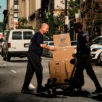 Two movers crossing the street with boxes on a dolly