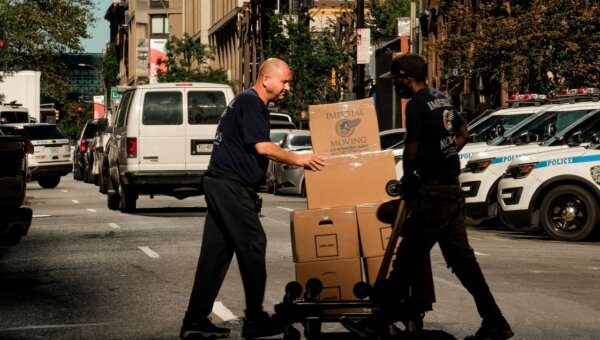 Two movers crossing the street with boxes on a dolly