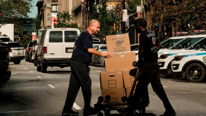 Two movers crossing the street with boxes on a dolly