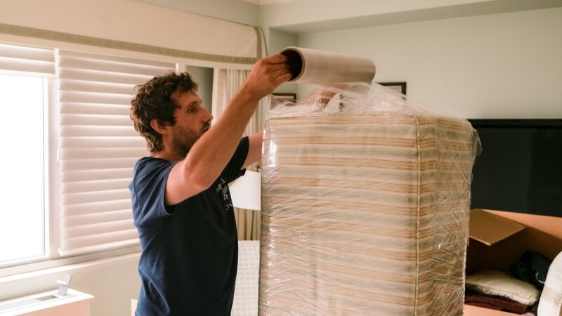 A professional mover wrapping a large item in plastic